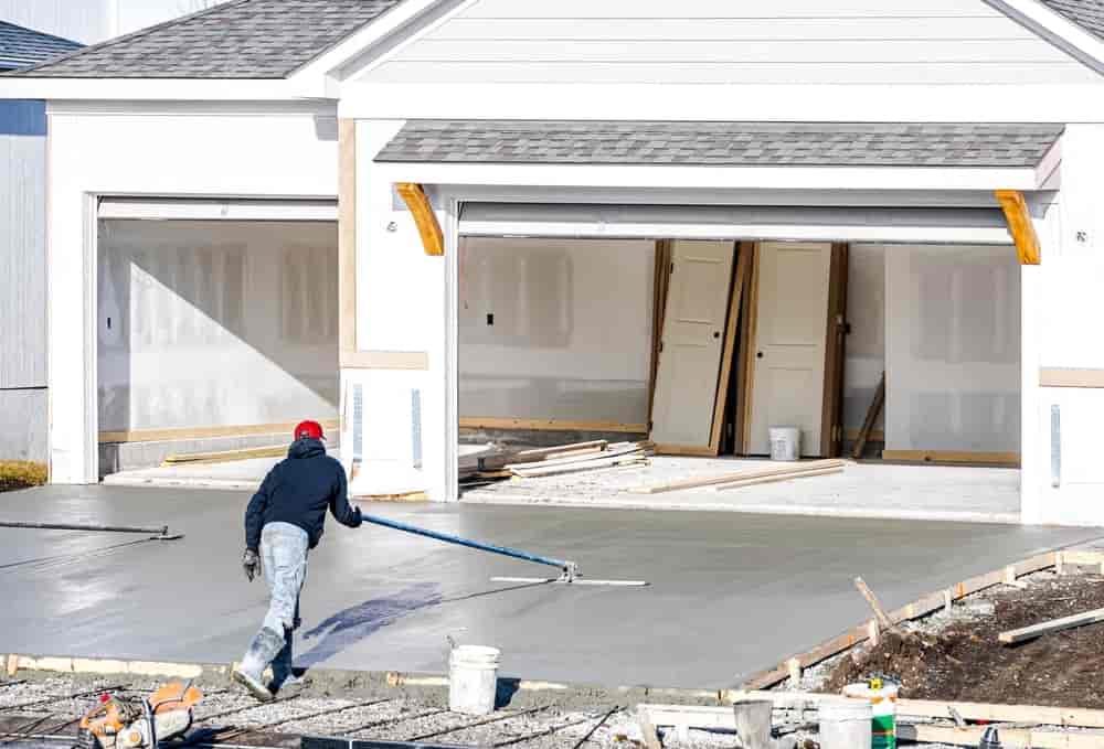Man working on smoothing concrete driveway for the new home build at construction site.